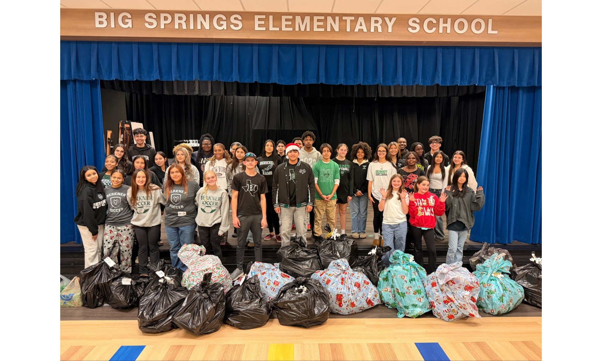 A group of Berkner High School athletes standing on a stage behind a massive pile of gift-wrapped presents.