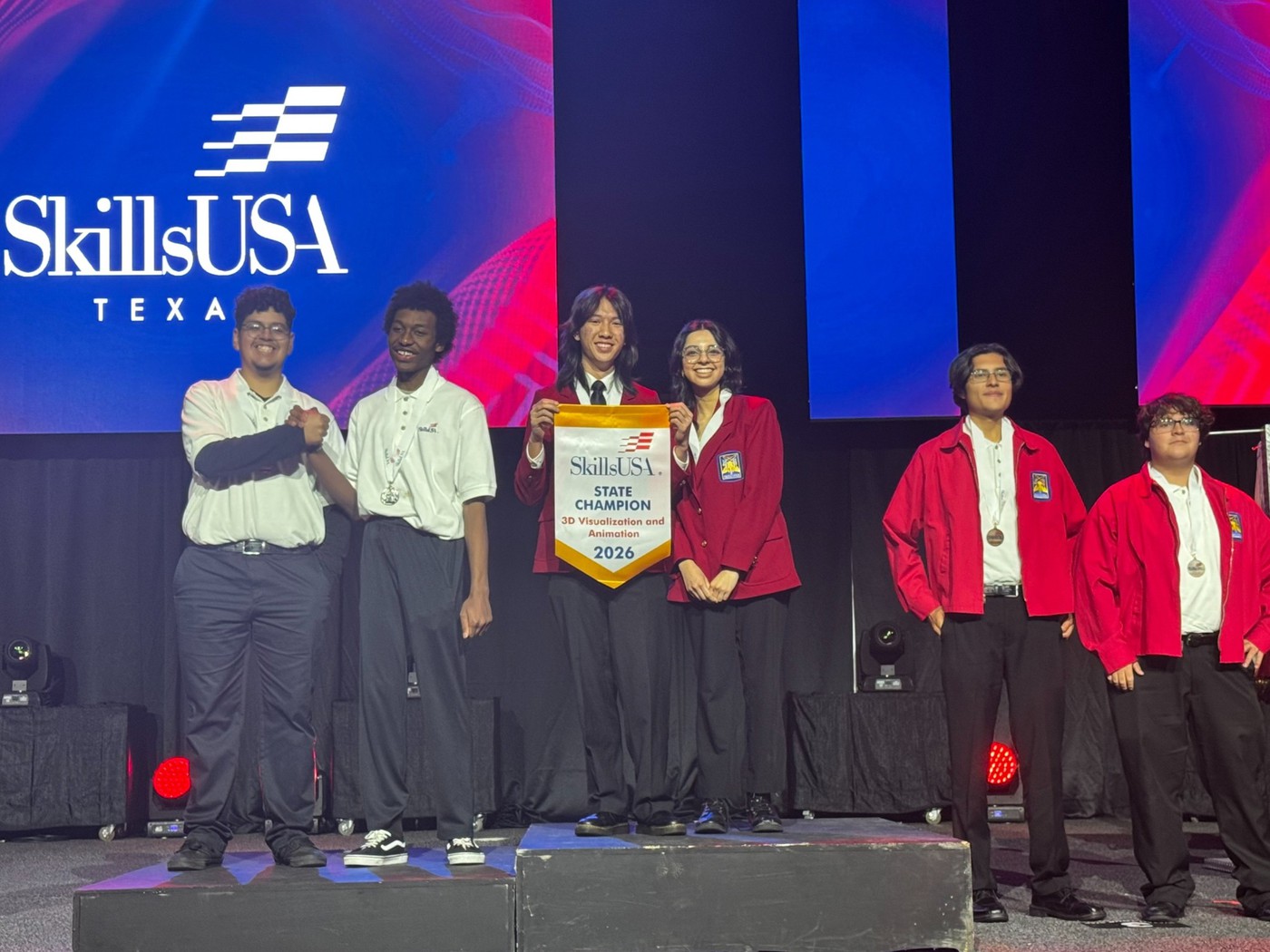 Berkner High School seniors Dat Nguyen and Lorena Araujo stand proudly on the first-place podium at the SkillsUSA Texas State competition. They are wearing official red SkillsUSA blazers and holding a yellow "State Champion" banner for 3D Visualization and Animation.