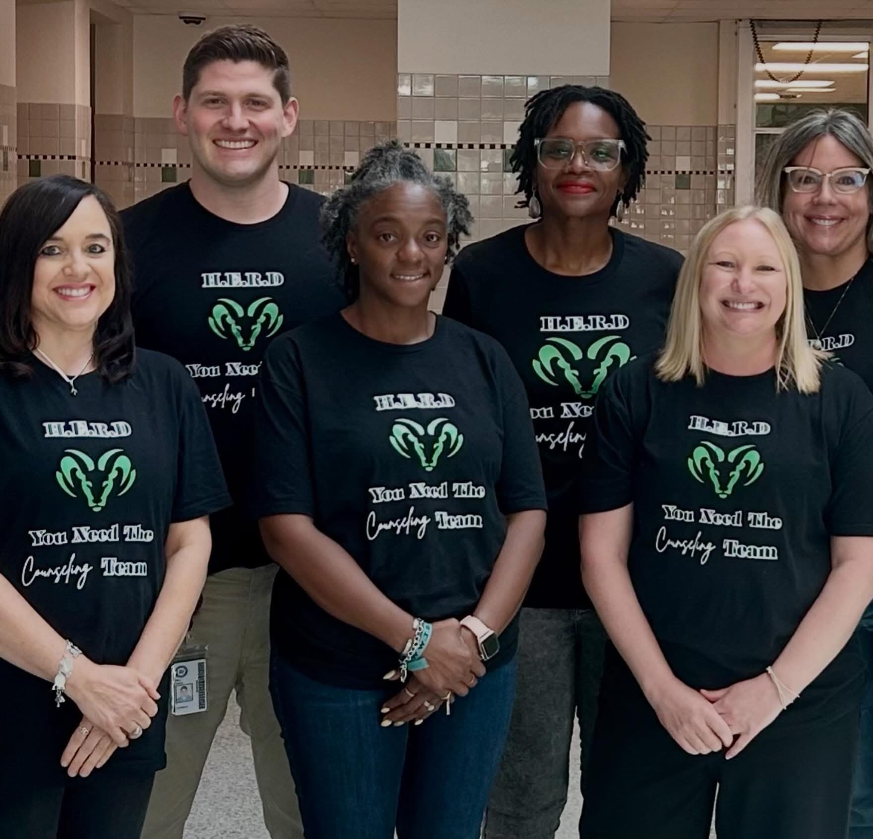 Six members of the Berkner High School counseling team smiling together in matching black t-shirts that feature a green ram logo and the phrase "H.E.R.D. You Need The Counseling Team".