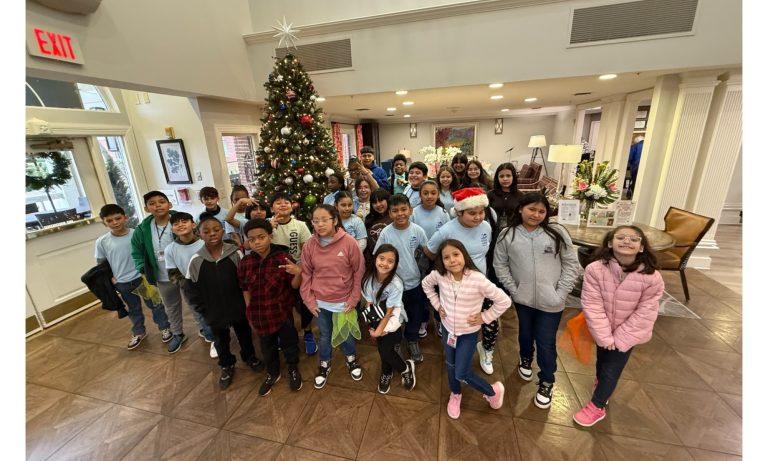 A group of Dover Elementary choir students standing in a lobby in front of a decorated Christmas tree.
