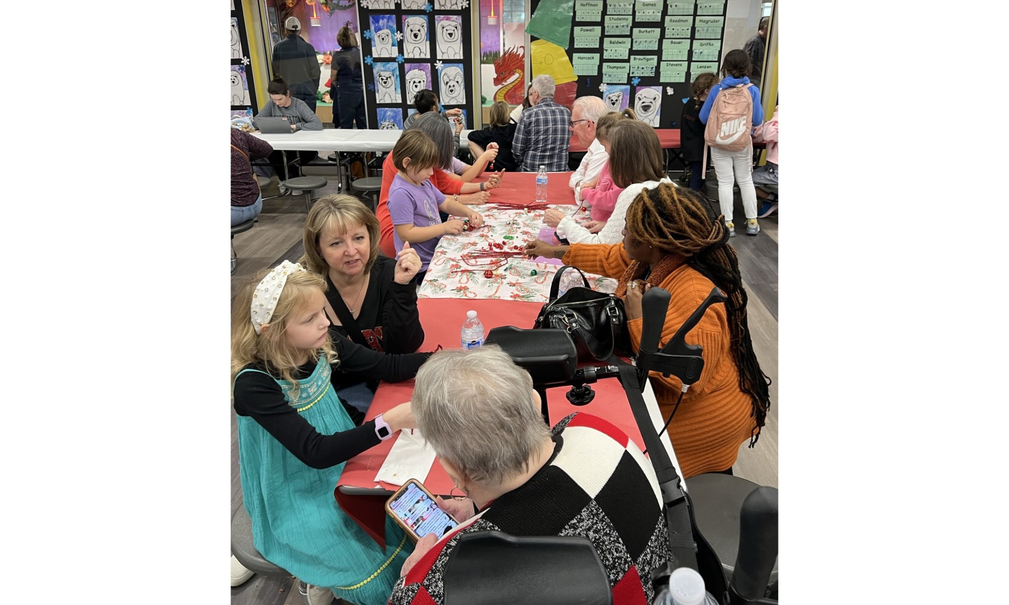 Students and their grandparents sitting at red tables in a cafeteria working on holiday crafts together.