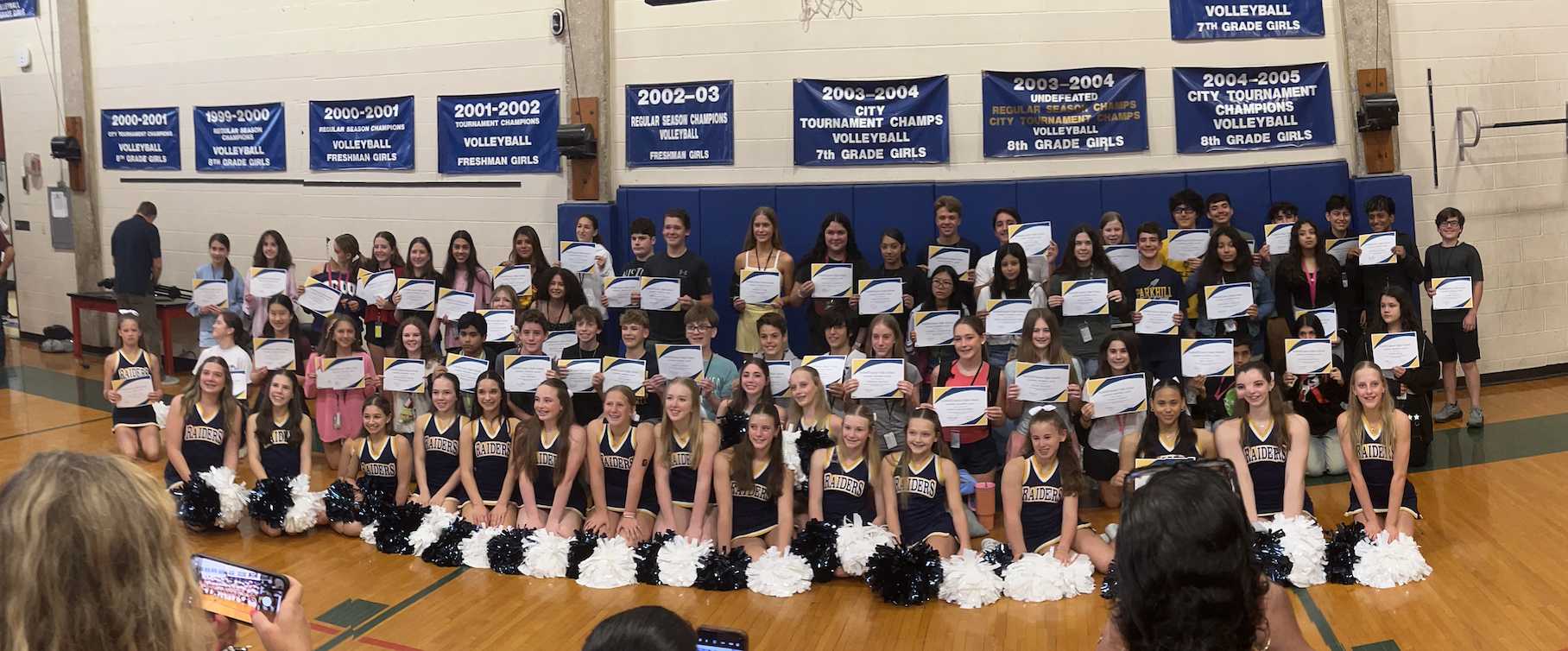 Students lined up in large gym holding award certificates