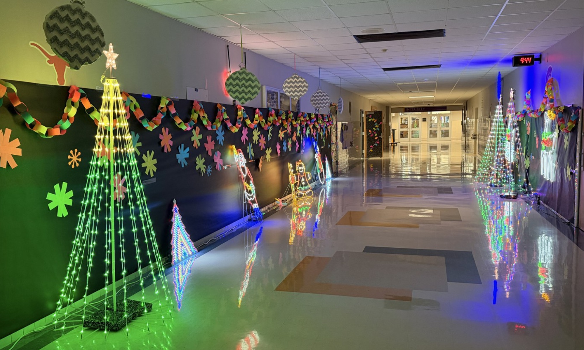 A school hallway illuminated by glowing green and white Christmas tree light displays.