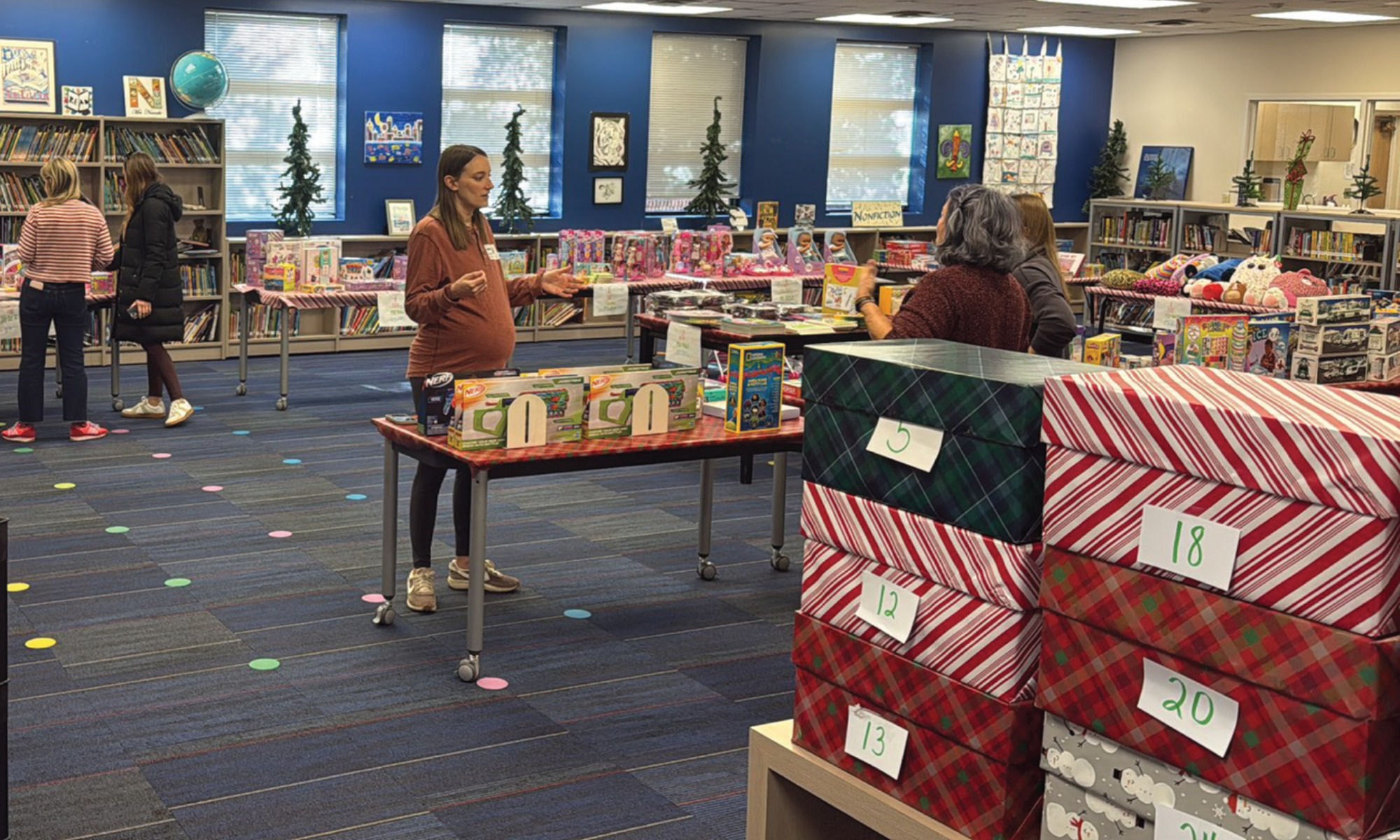 A school library filled with large, gift-wrapped boxes and holiday donations ready for distribution.