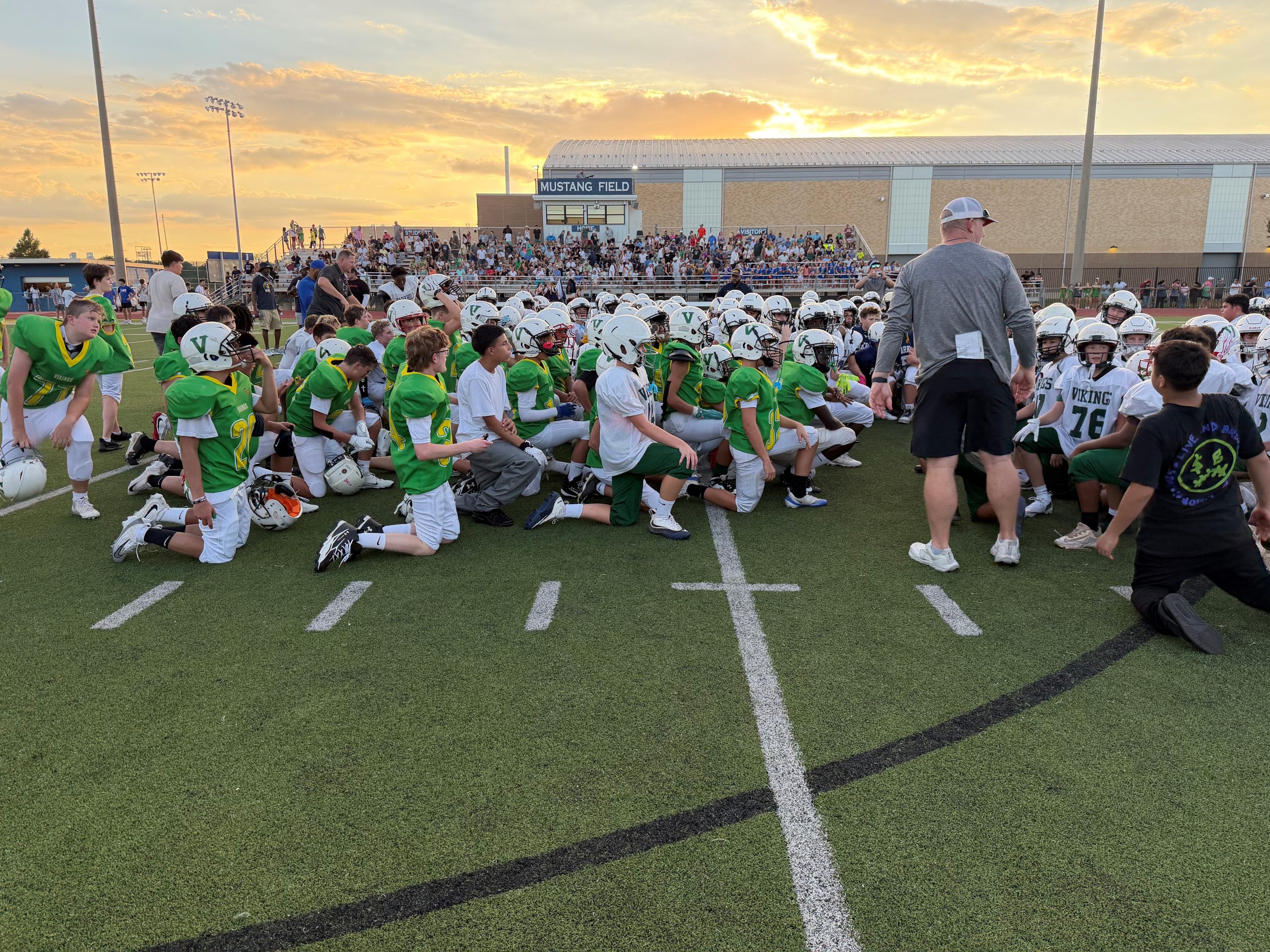 North football team in kneeled position on football field around coach.