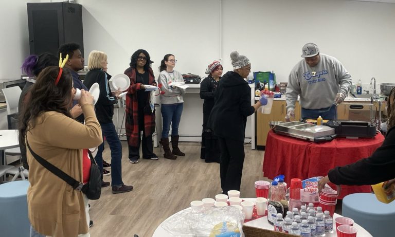 Parent volunteers standing behind a buffet table serving food to staff members in a school common area.