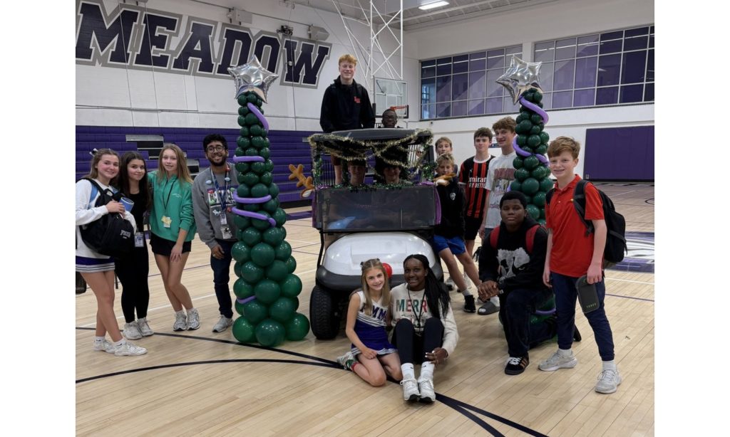 A group of students in a gym standing around a decorated holiday float during a school pep rally.